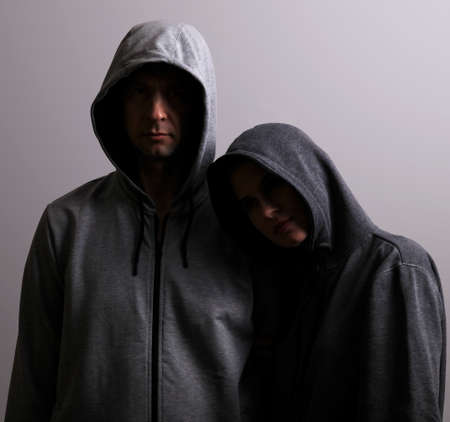 Male and female hooded hugs, low key, dark backgroundの写真素材