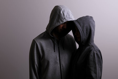 Male and female hooded hugs, low key, dark backgroundの写真素材