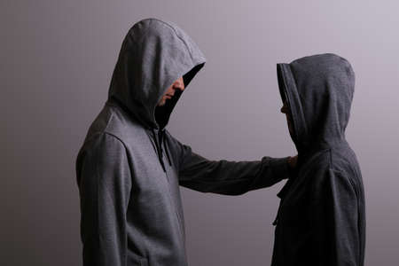 Man and woman in hoods stand by, low key, dark backgroundの写真素材