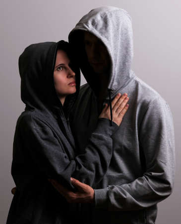 Male and female hooded hugs, low key, dark backgroundの写真素材