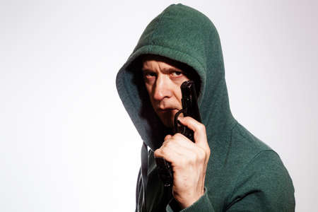 Hooded man with terrified look holds gun in handの写真素材