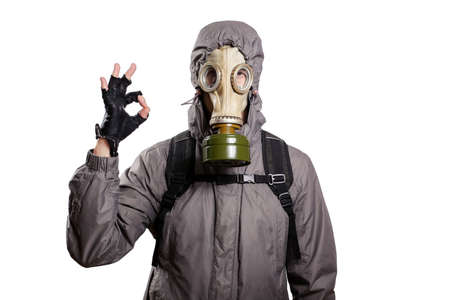An isolated shot of a man dressed in a gas mask, a hooded jacket, a backpack, shows a gesture of ok, looks into the camera. On a white isolated background, the studioの写真素材