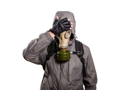 An isolated shot of a man dressed in a gas mask, a jacket with a hood, a backpack, put his hand on his head from grief and trouble. On a white isolated background, the studioの写真素材