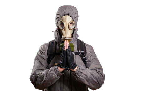 An isolated shot of a man dressed in a gas mask, a jacket with a hood, a backpack, praying, pressed the palms of his hands against each other. On a white isolated background, the studioの写真素材