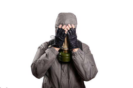 An isolated shot of a man dressed in a gas mask, a jacket with a hood, a backpack, covered his face with his hands from dissuasion and trouble. On a white isolated background, the studioの写真素材