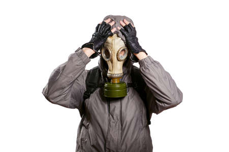 An isolated shot of a man dressed in a gas mask, a jacket with a hood, a backpack, grabbed his head with two hands out of regret and trouble. On a white isolated background, the studioの写真素材