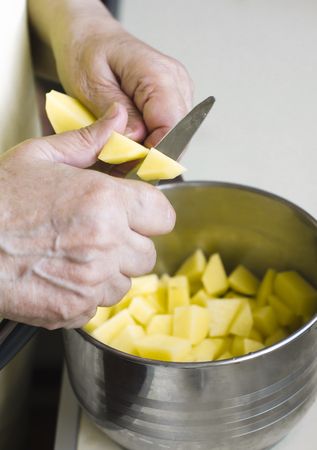 Grandma cuts potatoes a knife into a metal pan.の写真素材