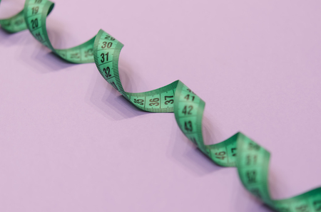 a green measuring tape twisted into a spiral lies on a purple background.の写真素材