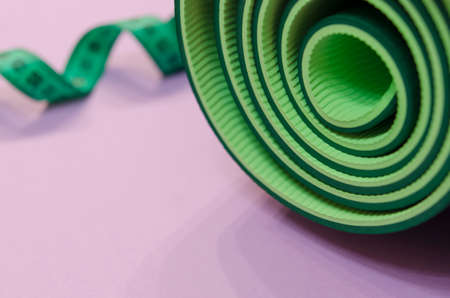 a green measuring tape twisted into a spiral and a mat for fitness lie on a purple background.の写真素材