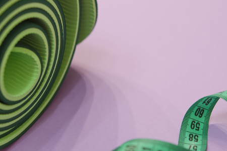 a green measuring tape twisted into a spiral and a mat for fitness lie on a purple background.の写真素材