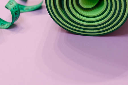 a green measuring tape twisted into a spiral and a mat for fitness lie on a purple background.の写真素材