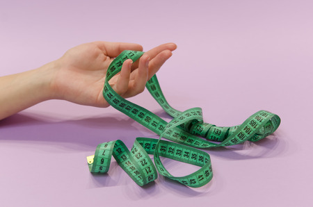 hand holding a green measuring tape on a purple background.の写真素材