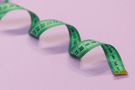 a green measuring tape twisted into a spiral lies on a purple background.