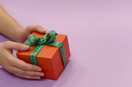 hands holding a gift box with a green measuring tape bow on a purple background.の写真素材