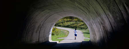 View of a dark tunnel in the public park with a male runnerの写真素材