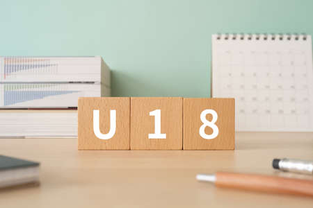 A desk with a building block with the word U18 written on it | an image of a person under the age of...