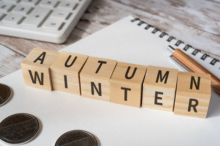 Wooden blocks with "AUTUMN" and "WINTER" text of concept, a calculator, coins, a notepad, and a pen.の写真素材