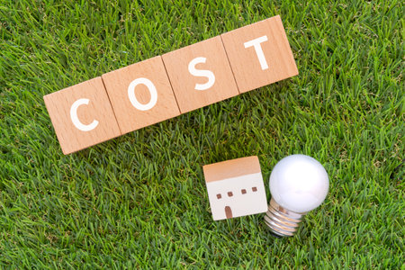 Wooden blocks with "COST" text of concept, a lightbulb, and a house toy.の写真素材