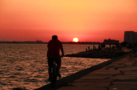 Silhouette of the cyclist riding a road bike at sunset. Sunset on the beach with beautiful sky. Egg Yolk Sunset.の写真素材