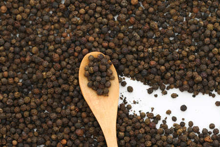 Black pepper on wooden spoon. Black peppercorn background. Black pepper background.