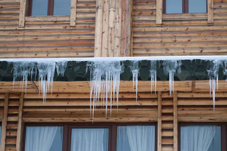 Large icicles on the roof of the wooden building. Fines for snow and ice on roofs.の写真素材