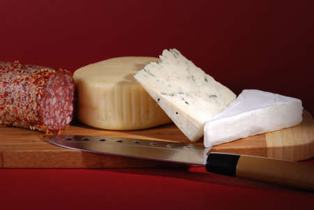 Cheese and salami still life against red background