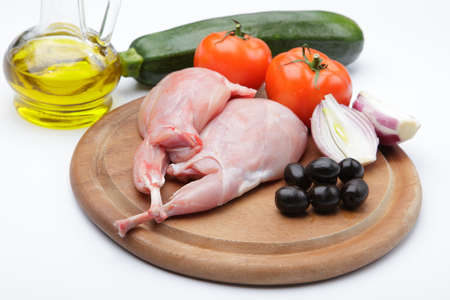 Raw rabbit legs with vegetables and olive oil on a wooden cutting boardの写真素材