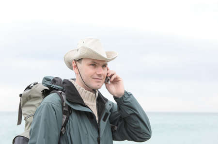 Man with backpack talking by phone against sea backgroundの写真素材