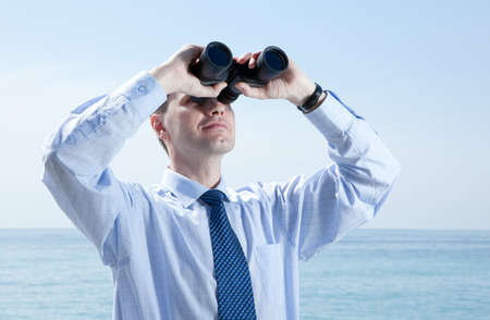 Businessman with binoculars against blue skyの写真素材