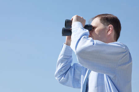 Businessman with binoculars against blue skyの写真素材