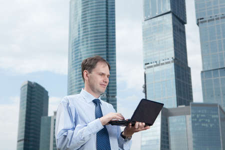 Businessman with laptop against modern buildingの写真素材