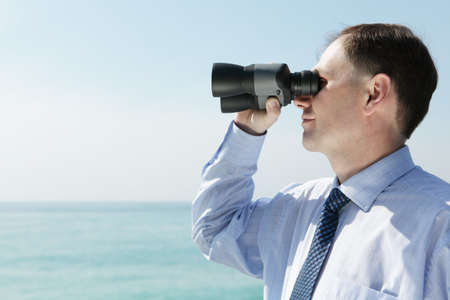 Businessman with binoculars against blue skyの写真素材