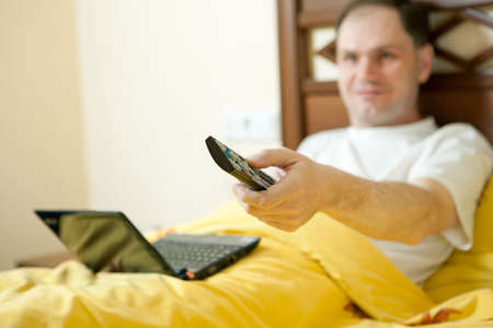 Man in the bed in hotel room with TV remote controlの写真素材