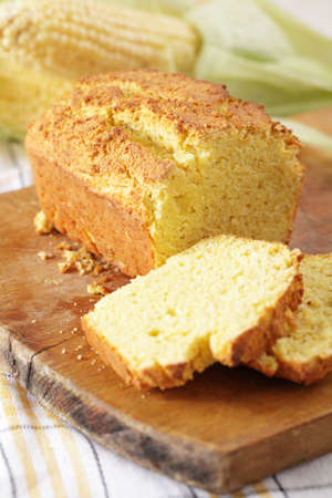 Corn bread on a cutting board against corn cobsの写真素材