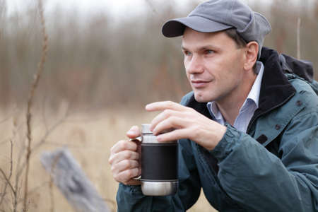 Man opening the mug with tea outdoors at the fallの写真素材