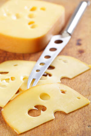 Sliced cheese and cheese knife on the wooden cutting boardの写真素材