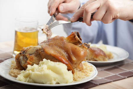 Man eating eisbein with braised cabbage, mashed potato, and beerの写真素材