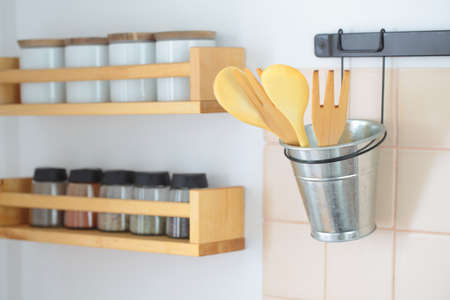 Wooden spatulas in a holder and racks with spices on a kitchen wallの写真素材