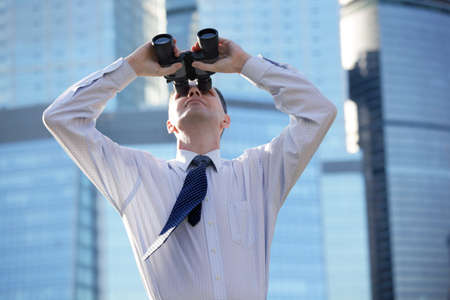 Businessman with binoculars against modern office buildingsの写真素材