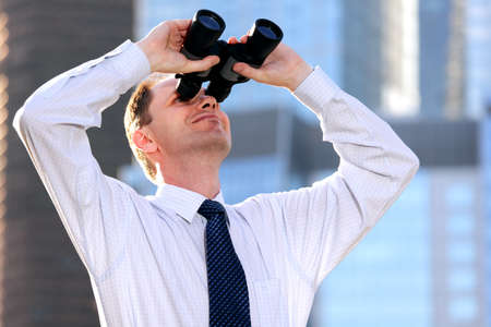 Businessman with binoculars against modern office buildingsの写真素材