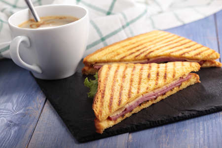 Sandwiches with ham, cheese, lettuce, grilled toasts, and a cup of coffee