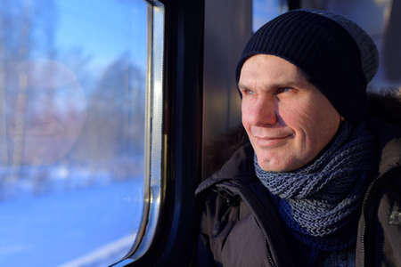 Mature man in winter clothes looks through the window in the commuter trainの写真素材