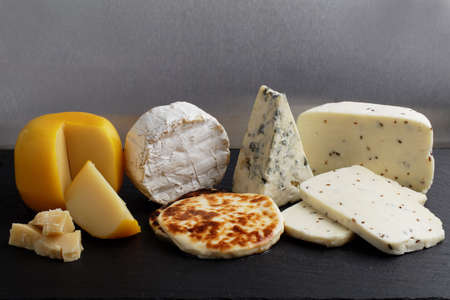 Collection of cheeses on a slate cutting board against gray backgroundの写真素材
