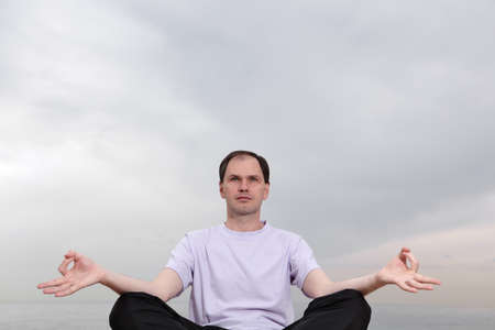 Mature man doing yoga against the seaの写真素材