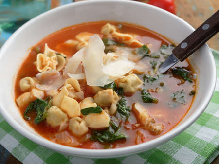 Tomato tortellini spinach soup with Parmesan cheese on a rustic tableの写真素材