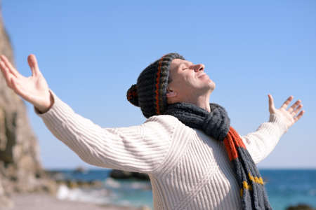 Happy man in knit hat and scarf on a beach under sun raysの写真素材