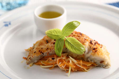 Baked breaded cod fish on vegetable bed topped with basil leaf