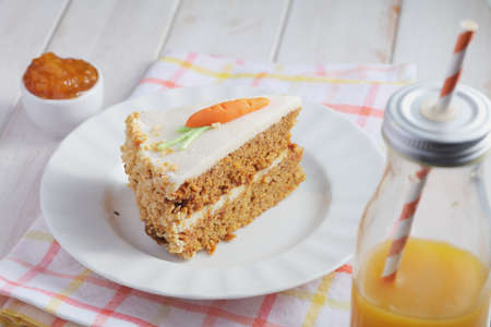 Slice of carrot cake  Pastel de zanahoria with icing and marzipan carrot on white background with carrot juice. Pastel colorsの写真素材