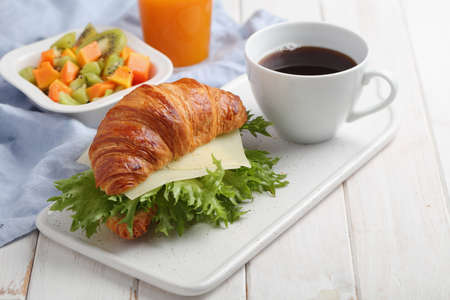 French breakfast: croissant sandwich with cheese, fruit salad, and a cup of black coffeeの写真素材