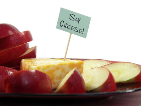Wedge of colorful cheese with a toothpick sign and apple slices on a red plate isolated on white. Shallow DOF, focus on sign.の写真素材